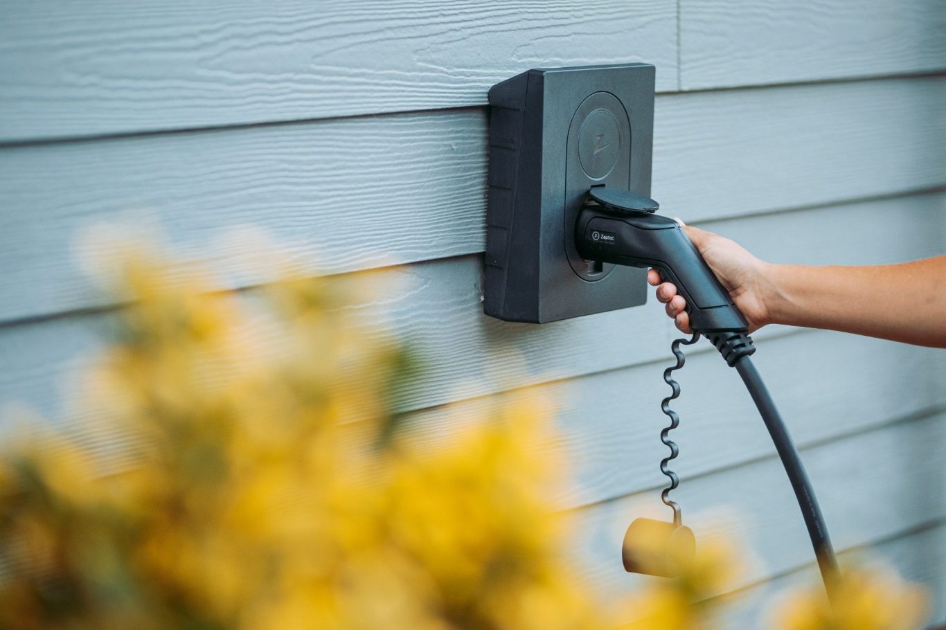 zaptec go Een hand steekt een laadkabel in een wandplug voor elektrische voertuigen.